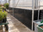 Black HDPE wall panels lining a long greenhouse nursery aisle with potting benches
