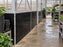 Black HDPE greenhouse wall panels along a long nursery walkway as a worker pushes a plant cart
