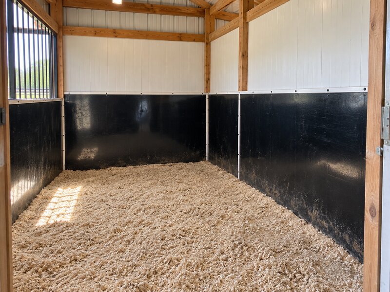 Black stall wall liner installed in a pole barn horse stall with white upper wall panels
