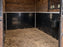Black stall wall liner beneath a white-paneled stall wall with a wall-mounted hay rack
