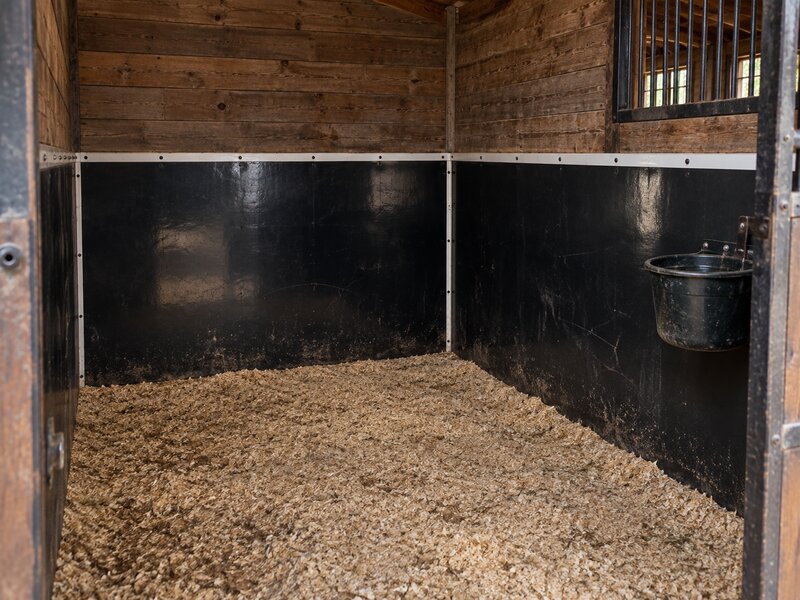 Black stall wall liner beneath a white-paneled stall wall with a wall-mounted hay rack
