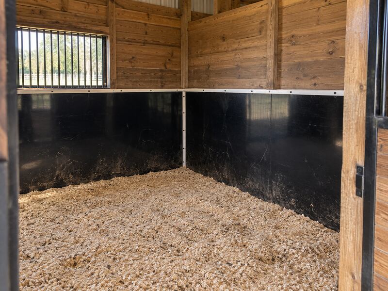 Black stall wall liner installed in a wood-paneled horse stall corner with natural light
