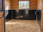 Black HDPE horse stall wall liner installed on the lower walls of a wood-paneled stall with a barred window
