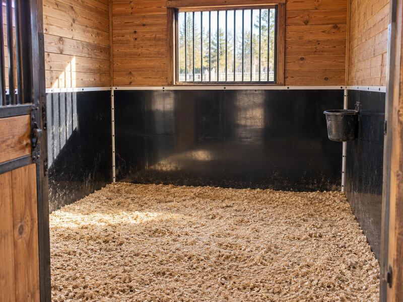 Black HDPE horse stall wall liner installed on the lower walls of a wood-paneled stall with a barred window
